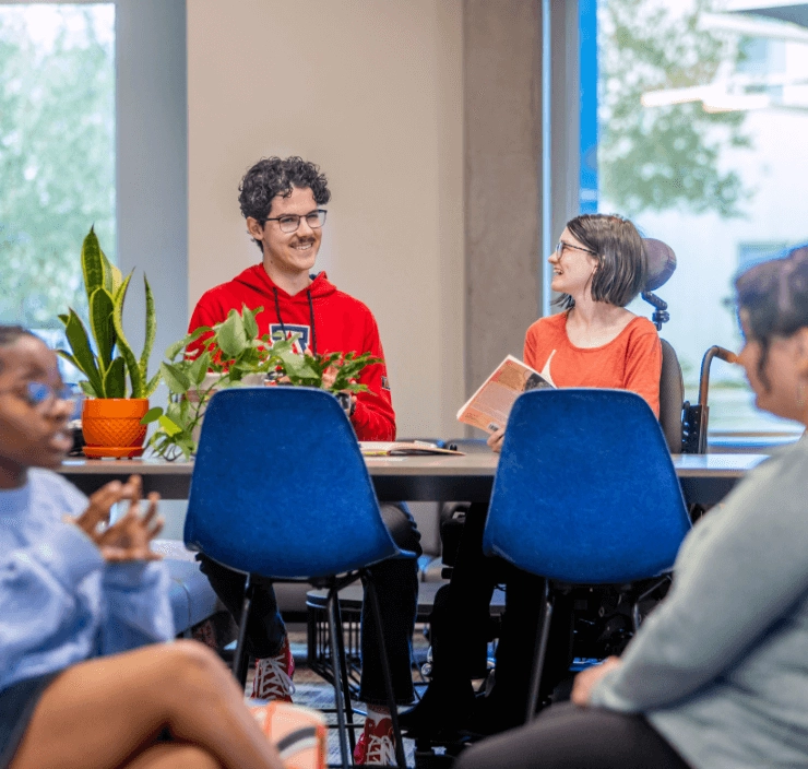 2 students smiling, 1 seated in a wheelchair